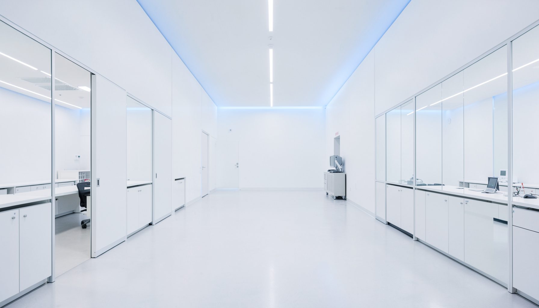 A clean architectural photograph of a modern research laboratory interior with strong symmetry, white surfaces, and soft blue accent lighting