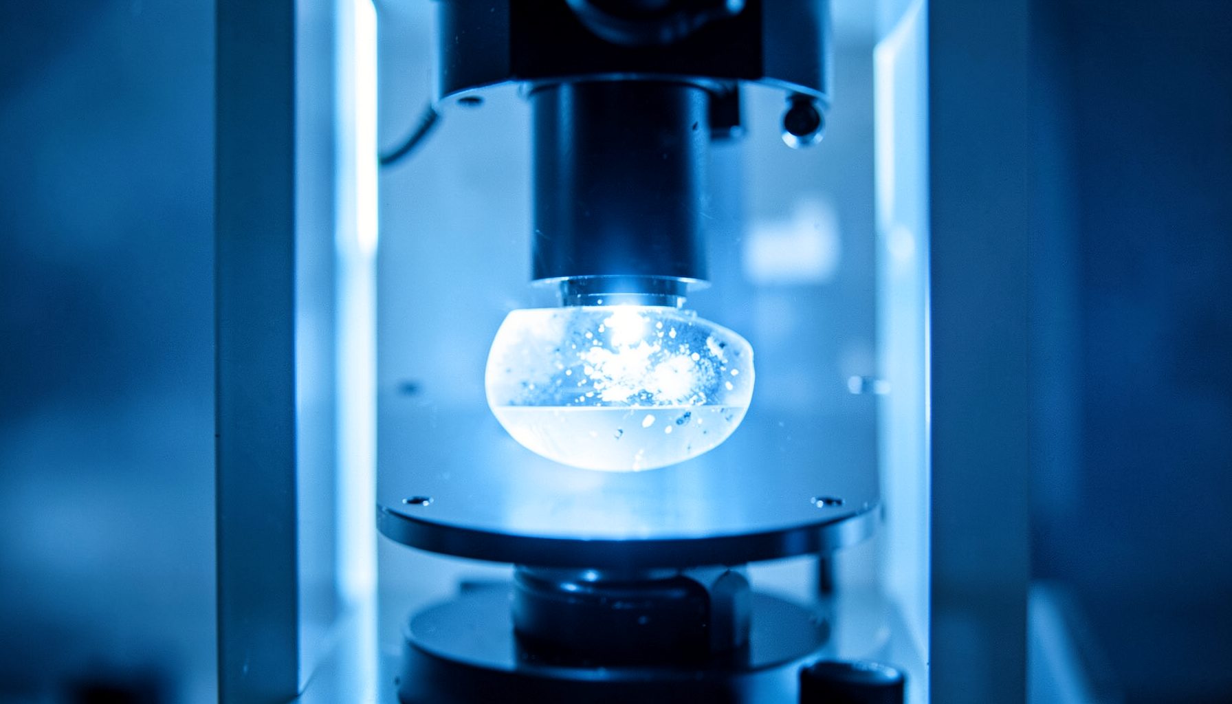 Close-up of a laboratory microscope with a glowing specimen slide, cool blue and white tones dominating the frame